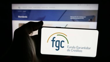 Stuttgart, Almanya - 11-28-2025: İnternet sayfasının önünde Brezilya 'nın Fundo Garantidor de Creditos (FGC) logosu olan cep telefonu sahibi kişi. Telefon ekranına odaklan.