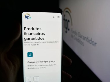 Stuttgart, Almanya - 11-28-2025: Brezilyalı Fundo Garantidor de Creditos 'un (FGC) web sayfası logonun önünde duran kişi. Telefon ekranının merkezine odaklan.