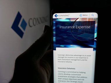 Stuttgart, Almanya - 11-28-2025: Yatırım şirketi Conning Holding Limited 'in web sayfası logonun önünde duran kişi. Telefon ekranının merkezine odaklan.