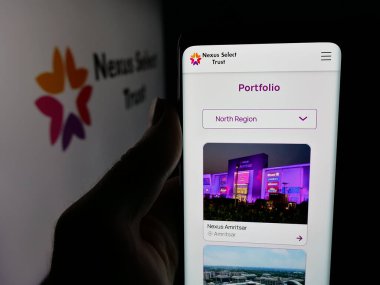 Stuttgart, Almanya - 11-30-2025: Hintli emlak şirketi Nexus Select Trust 'ın internet sayfası ile logo önünde cep telefonu tutan kişi. Telefon ekranının merkezine odaklan.