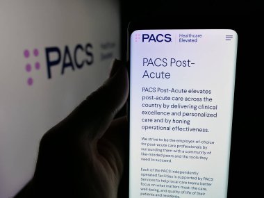 Stuttgart, Almanya - 11-30-2025: ABD 'li sağlık şirketi PACS Group Inc.' in web sayfası ile akıllı telefon sahibi kişi logonun önünde ekranda. Telefon ekranının merkezine odaklan.