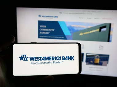 Stuttgart, Almanya - 12-01-2025: Finans hizmetleri şirketi Westamerica Bank 'ın logosuna sahip akıllı telefonu web sitesinin önünde ekranda tutan kişi. Telefon ekranına odaklan.