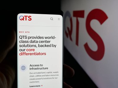 Stuttgart, Almanya - 12-05-2025: ABD veri merkezi şirketi QTS Emlak Tröstü LLC 'nin web sayfası ile akıllı telefon sahibi kişi logonun önünde ekranda. Telefon ekranının merkezine odaklan.