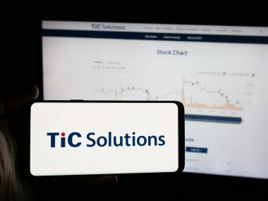 Stuttgart, Almanya - 12-05-2025: İnternet sitesinin önünde üzerinde test şirketi TIC Solutions Inc. 'in logosu bulunan akıllı telefon sahibi kişi. Telefon ekranına odaklan.