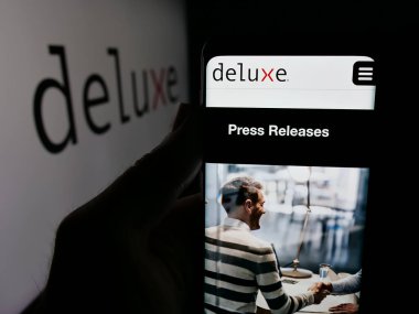 Stuttgart, Almanya - 12-08-2025: ABD 'li finans şirketi Deluxe Corporation' ın web sitesiyle akıllı telefon sahibi kişi logonun önünde ekranda. Telefon ekranının merkezine odaklan.