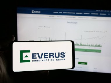 Stuttgart, Almanya - 12-10-2025: ABD 'li Everus İnşaat Grubu Inc. şirketinin logosunu elinde tutan kişi web sitesinin önünde ekranda. Telefon ekranına odaklan.