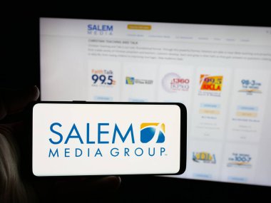 Stuttgart, Almanya - 12-11-2025: İnternet sitesi önünde ekranda ABD 'li radyo şirketi Salem Media Group Inc.' in logosunun bulunduğu akıllı telefon sahibi kişi. Telefon ekranına odaklan.