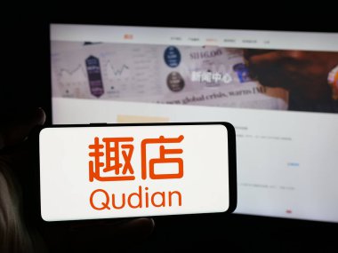 Stuttgart, Almanya - 12-12-2025: Çinli teknoloji şirketi Qudian Inc. 'in logosunu elinde tutan kişi web sitesinin önünde ekranda. Telefon ekranına odaklan.