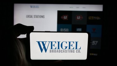 Stuttgart, Almanya - 12-12-2025: ABD 'li televizyon şirketi Weigel Broadcasting Co' nun logosunun bulunduğu cep telefonu web sayfası önünde ekranda. Telefon ekranına odaklan.