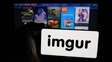 Stuttgart, Almanya - 12-12-2025: Web sayfası önünde ekranda ABD imaj paylaşım topluluğu Imgur 'un (Imgur.com) logosuna sahip cep telefonu bulunan kişi. Telefon ekranına odaklan.