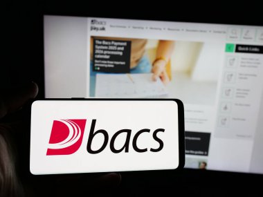 Stuttgart, Almanya - 12-16-2025: İngiliz şirketi Bacs Payment Schemes Limited 'in logosuna sahip akıllı telefon sahibi kişi web sitesi önünde ekranda. Telefon ekranına odaklan.