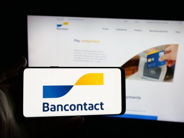 Stuttgart, Germany - 12-16-2025: Person holding smartphone with logo of Belgian financial services company Bancontact on screen in front of website. Focus on phone display.