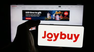 Stuttgart, Almanya - 12-17-2025: İnternet sayfası önünde üzerinde e-ticaret şirketi Joybuy (Joybuy.com) logosu bulunan cep telefonu sahibi kişi. Telefon ekranına odaklan.