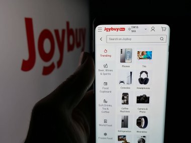 Stuttgart, Almanya - 12-17-2025: Logo önündeki ekranda e-ticaret şirketi Joybuy 'ın (Joybuy.com) web sayfası ile cep telefonu tutan kişi. Telefon ekranının merkezine odaklan.