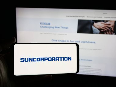 Stuttgart, Almanya - 12-17-2025: Japon elektronik şirketi Sun Corporation 'ın logosunu elinde tutan kişi web sitesinin önünde ekranda. Telefon ekranına odaklan.