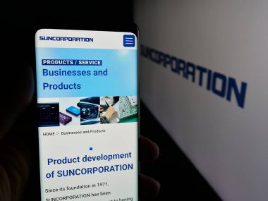 Stuttgart, Almanya - 12-17-2025: Japon elektronik şirketi Sun Corporation 'ın web sayfası ile logo önünde cep telefonu tutan kişi. Telefon ekranının merkezine odaklan.
