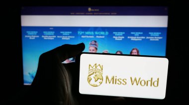 Stuttgart, Almanya - 12-18-2025: Güzellik yarışması organizasyonu logosu olan cep telefonu sahibi kişi web sayfasının önünde ekranda. Telefon ekranına odaklan.