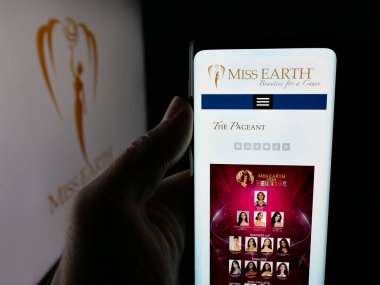 Stuttgart, Almanya - 12-18-2025: Güzellik yarışması organizasyonu Miss Earth 'ün internet sayfası olan cep telefonunu logonun önünde tutan kişi. Telefon ekranının merkezine odaklan.