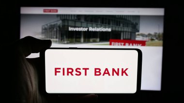 Stuttgart, Almanya - 12-18-2025: Finans şirketi First Bank 'ın (LocalFirstBank) logosuna sahip cep telefonu web sayfası önünde ekranda. Telefon ekranına odaklan.