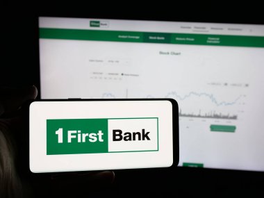 Stuttgart, Almanya - 12-18-2025: Finans şirketi First Bancorp 'un (FirstBank) logosunu elinde bulunduran kişi web sitesinin önünde ekranda. Telefon ekranına odaklan.