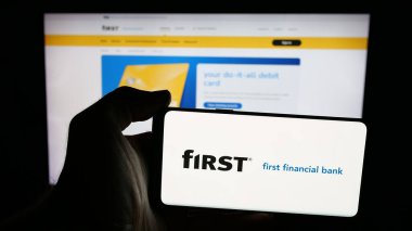 Stuttgart, Almanya - 12-18-2025: İnternet sayfası önünde First Financial Bancorp (Bankatfirst) şirketinin logosunun bulunduğu cep telefonu sahibi kişi. Telefon ekranına odaklan.