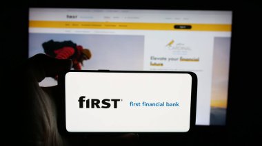 Stuttgart, Almanya - 12-18-2025: İnternet sayfası önünde First Financial Bancorp (Bankatfirst) şirketinin logosunu elinde tutan kişi. Telefon ekranına odaklan.