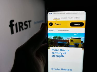 Stuttgart, Almanya - 12-18-2025: Logo önünde First Financial Bancorp (Bankatfirst) şirketinin web sayfası ile cep telefonu tutan kişi. Telefon ekranının merkezine odaklan.