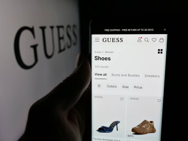 Stuttgart, Almanya - 12-19-2025: ABD 'li giyim şirketi Guess Inc.' in web sayfası olan cep telefonu logonun önünde ekranda. Telefon ekranının merkezine odaklan.