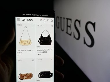 Stuttgart, Almanya - 12-19-2025: ABD 'li giyim şirketi Guess Inc.' in web sayfası olan akıllı telefon sahibi kişi logonun önünde ekranda. Telefon ekranının merkezine odaklan.