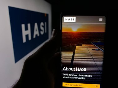 Stuttgart, Almanya - 01-15-2026: ABD 'li altyapı sermaye şirketi HASI' nin web sitesi ile akıllı telefonu logo önünde ekranda tutan kişi. Telefon ekranının merkezine odaklan.