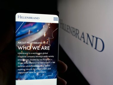 Stuttgart, Almanya - 01-16-2026: ABD 'li endüstri şirketi Hillenbrand Inc.' in web sitesiyle akıllı telefon sahibi kişi logonun önünde ekranda. Telefon ekranının merkezine odaklan.