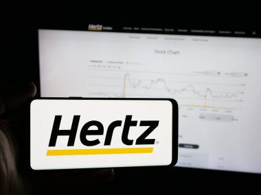 Stuttgart, Almanya - 01-19-2026: Araba kiralama şirketi Hertz Global Holding Inc. 'nin logosunu taşıyan akıllı telefon sahibi kişi web sitesinin önünde ekranda. Telefon ekranına odaklan.