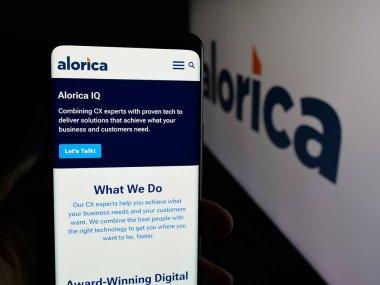Stuttgart, Almanya - 01-22-2026: ABD 'li müşteri deneyimi şirketi Alorica Inc.' in internet sayfası ile cep telefonu tutan kişi logonun önünde ekranda. Telefon ekranının merkezine odaklan.
