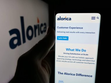 Stuttgart, Almanya - 01-22-2026: ABD 'li müşteri deneyimi şirketi Alorica Inc.' in web sayfası ile akıllı telefon sahibi kişi logo önünde ekranda. Telefon ekranının merkezine odaklan.