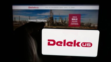 Stuttgart, Almanya - 01-26-2026: Petrol arıtma şirketi Delek US Holding Inc. 'in logosunu taşıyan cep telefonu sahibi kişi web sayfasının önünde ekranda. Telefon ekranına odaklan.