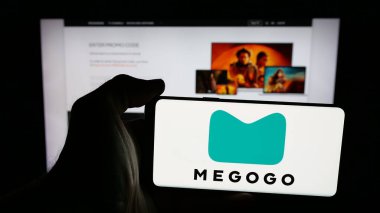 Stuttgart, Almanya - 02-02-2026: Web sayfasının önünde ekranda video yayın platformu şirketi Megogo 'nun logosuna sahip cep telefonu tutan kişi. Telefon ekranına odaklan.