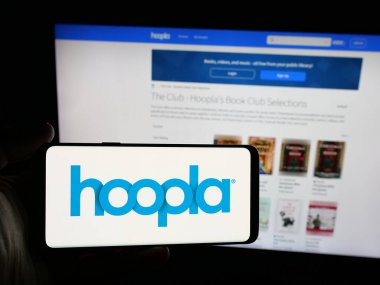 Stuttgart, Almanya - 02-02-2026: İnternet sitesi önünde ekranda ABD 'li yayın platformu şirketi Hoopla Digital' in logosuna sahip akıllı telefon sahibi kişi. Telefon ekranına odaklan.