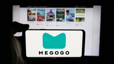 Stuttgart, Almanya - 02-02-2026: Web sayfası önünde ekranda video yayın platformu şirketi Megogo 'nun logosuna sahip cep telefonu tutan kişi. Telefon ekranına odaklan.
