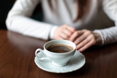 Açık bir fincanda kahve ve tabağın üzerinde açık renk ceketli bir kızın önünde.