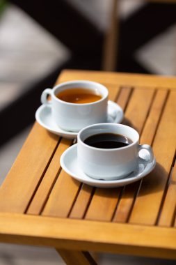 Güneşli bir sabahta evin verandasındaki ahşap bir masada bir fincan kahve ve bir fincan çay.