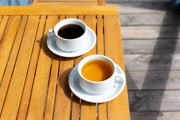 Güneşli bir sabahta evin verandasındaki ahşap bir masada bir fincan kahve ve bir fincan çay.