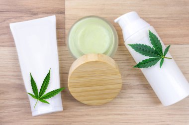 Flat lay of CBD lotion in glass container with Cannabis leaf on wooden backdrop with copy space