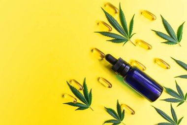 Sarı zemin üzerinde CBD Cannabidiol şişe kapsülleri ve kenevir yaprakları, alternatif tıp konsepti