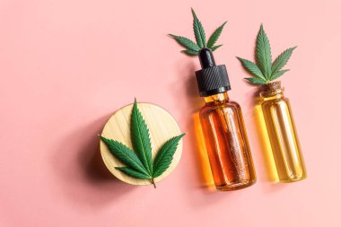 CBD Cannabidiol yağ şişeleri Kenevir kremi ve pembe arka planda kenevir yaprakları