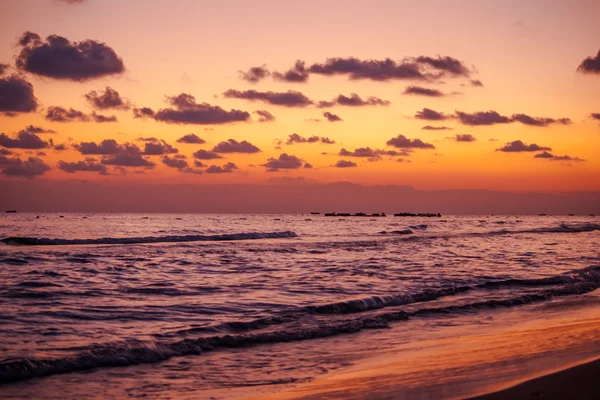 Dalgalar deniz üzerinde bir plaj renkli bir gün batımı sırasında.