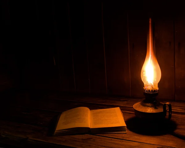 Antiguo libro antiguo abierto con lámpara de parafina ardiente cerca de la mesa de madera . —  Fotos de Stock