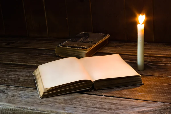 Viejo libro antiguo abierto con vela encendida cerca de la mesa de madera. Página en blanco Imagen de stock