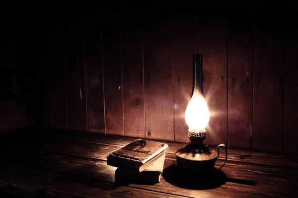 Libros antiguos con lámpara de parafina ardiente cerca de la mesa de madera . Fotos de stock libres de derechos