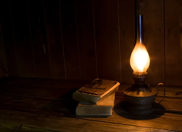 Old antique books with burning paraffin lamp near on the wooden table. — Stock Photo, Image
