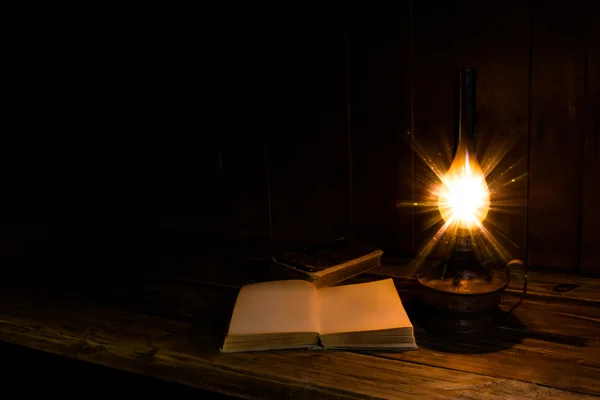 Libros antiguos con lámpara de parafina ardiente cerca de la mesa de madera — Foto de Stock